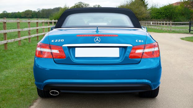 Rear view of a blue luxury convertible parked by a wooden fence, showcasing elegance and nature.